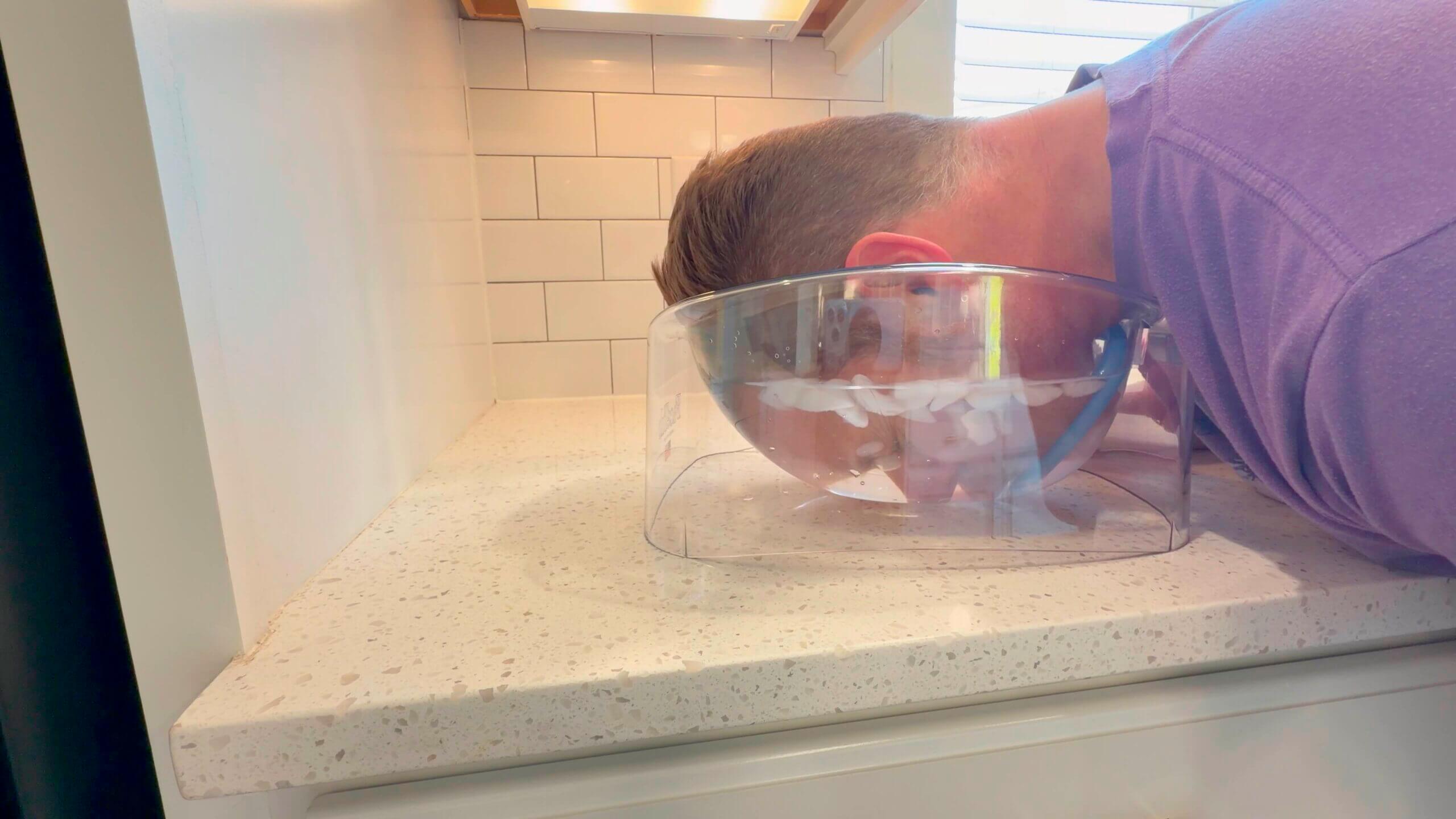 FaceTub face cold plunge therapy device with clear acrylic bowl and blue snorkel breathing mask on countertop for facial ice bath immersion and cold water therapy treatment